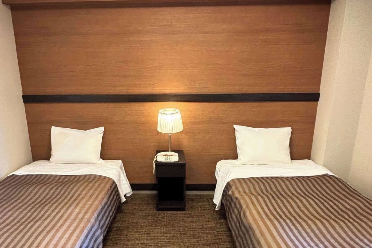 Una habitación de hotel con dos camas individuales, una mesita de noche con lámpara y cabecero de madera.