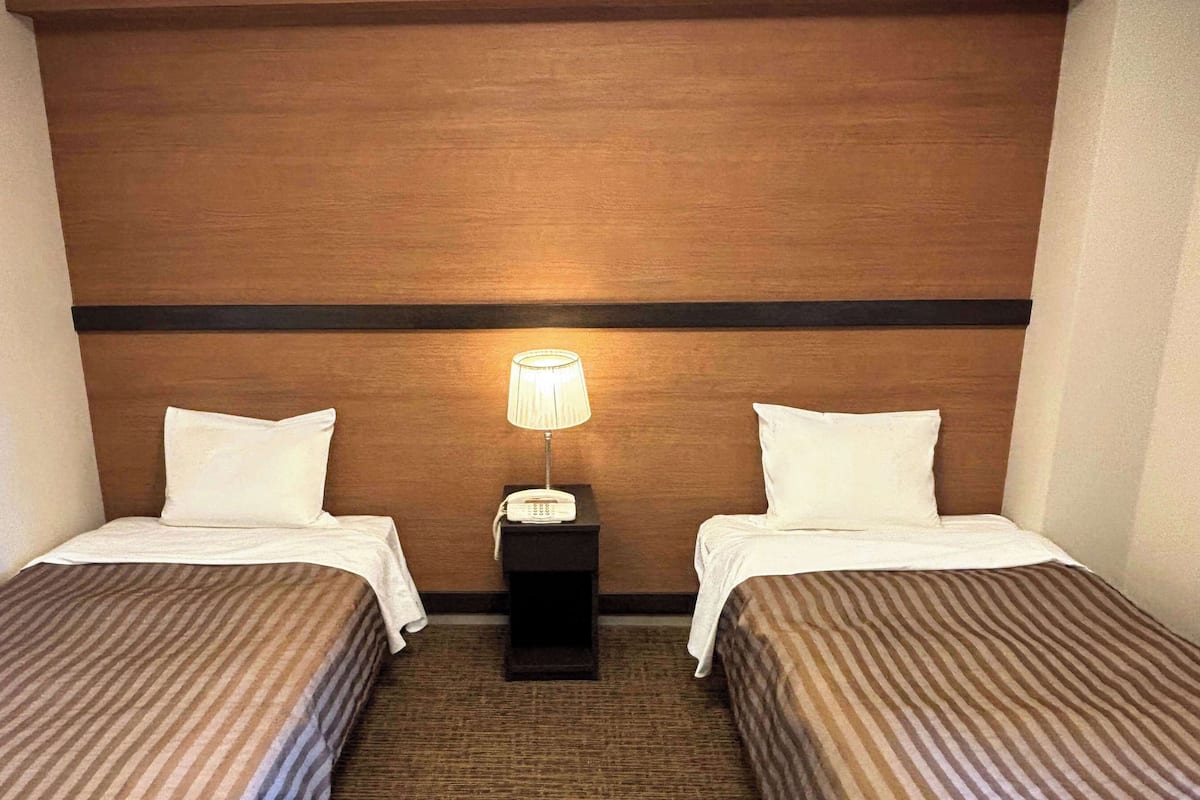 A hotel room with two single beds, a nightstand with a lamp, and a wooden headboard.