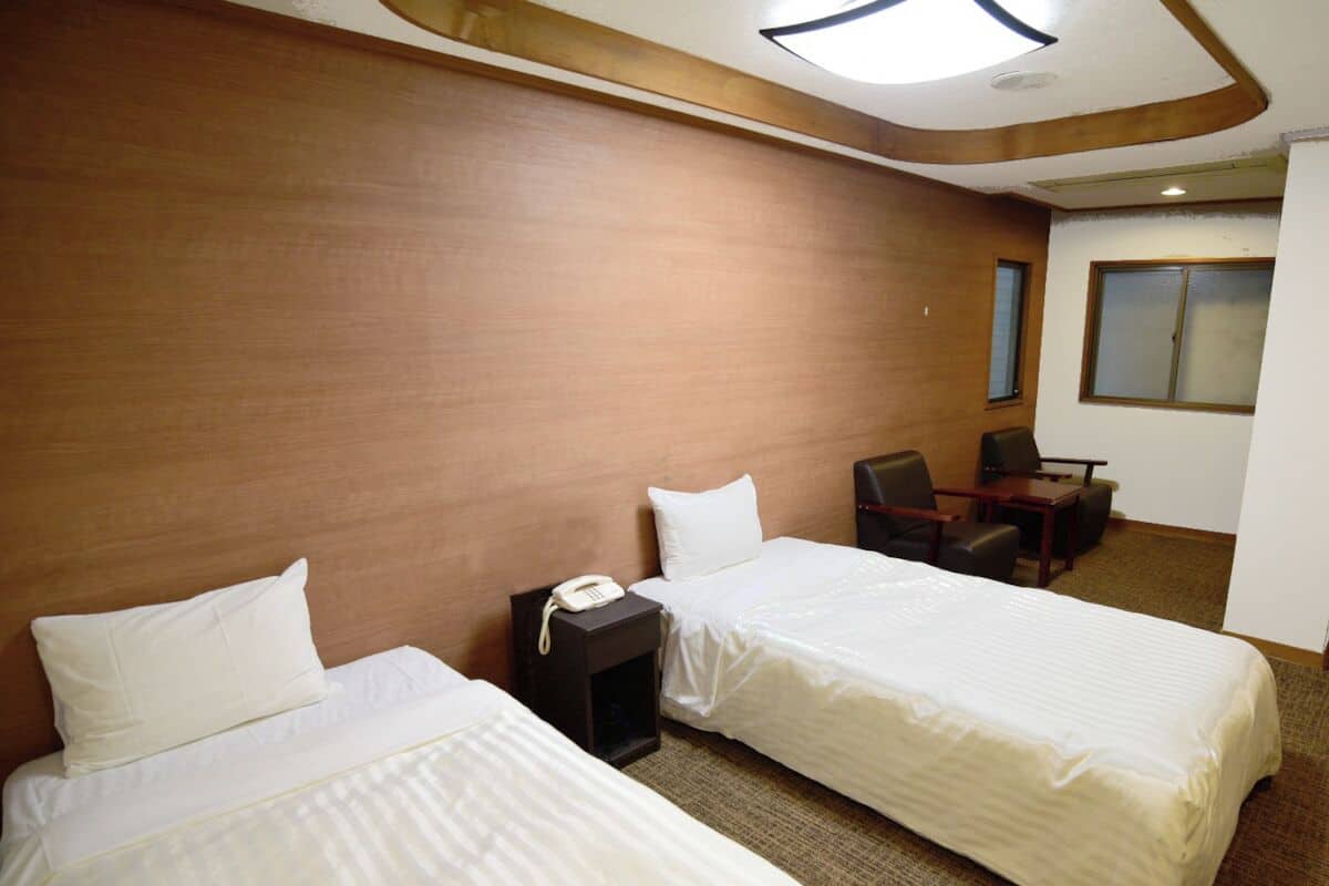 A hotel room with two beds, a desk, a chair, and a telephone.