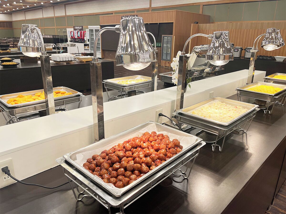 A buffet area with various food items in trays, buffet lights, and a counter.