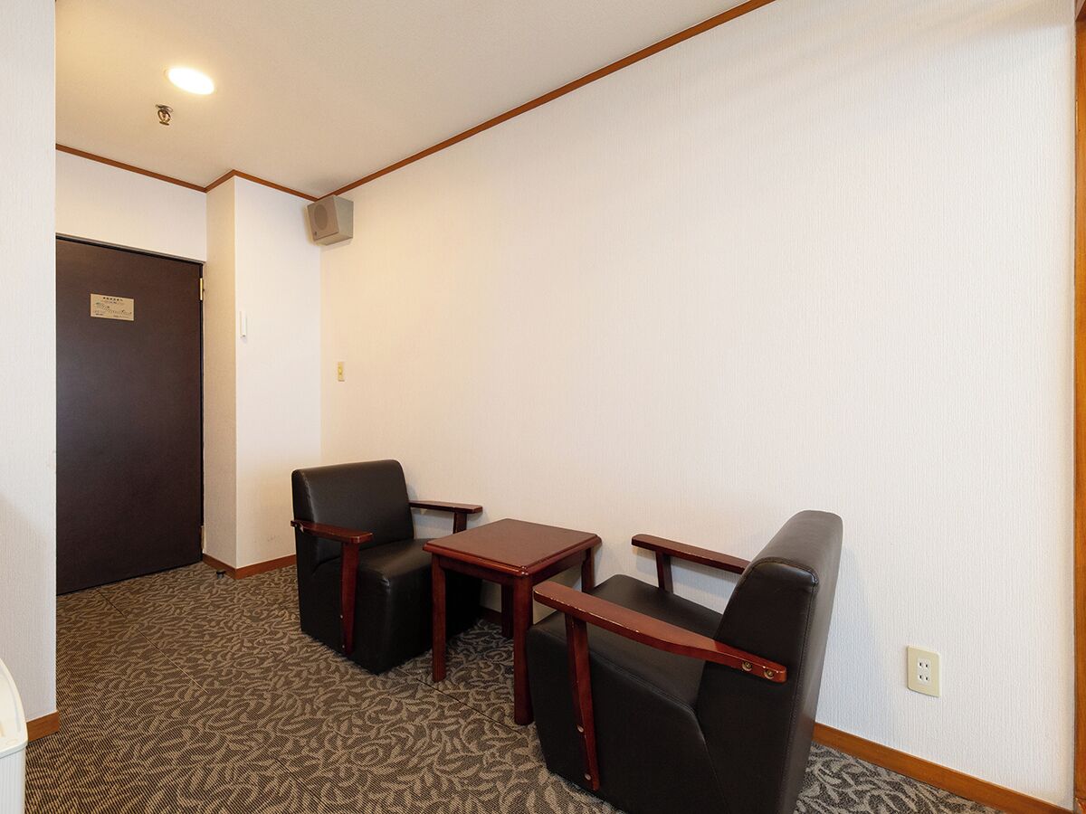 Habitación de hotel con dos sillones de cuero negro, una mesita de madera y piso alfombrado.