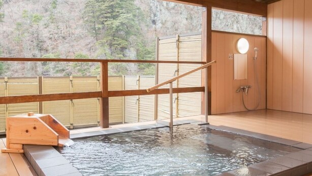 Un onsen japonés tradicional con terraza de madera, un baño de aguas termales y una sauna de madera.