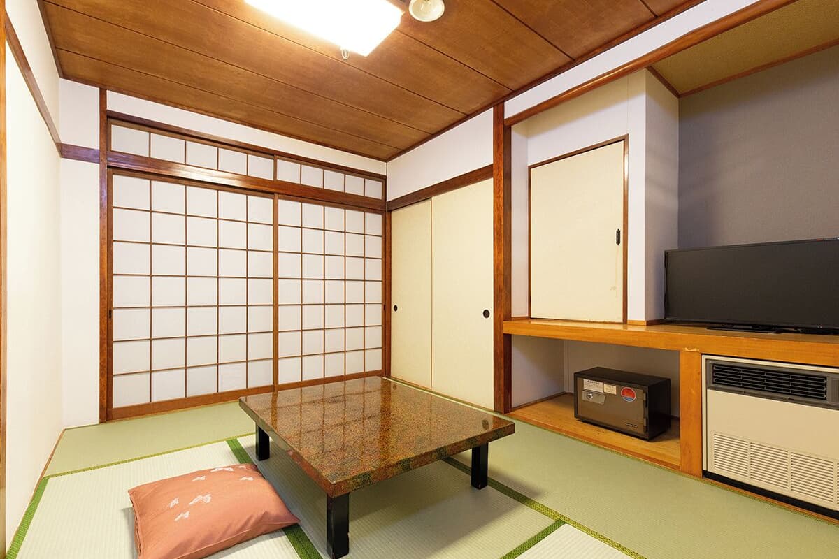 Ett traditionellt japanskt rum med tatamimattor på golvet, ett lågt bord, en tv och ett skåp.