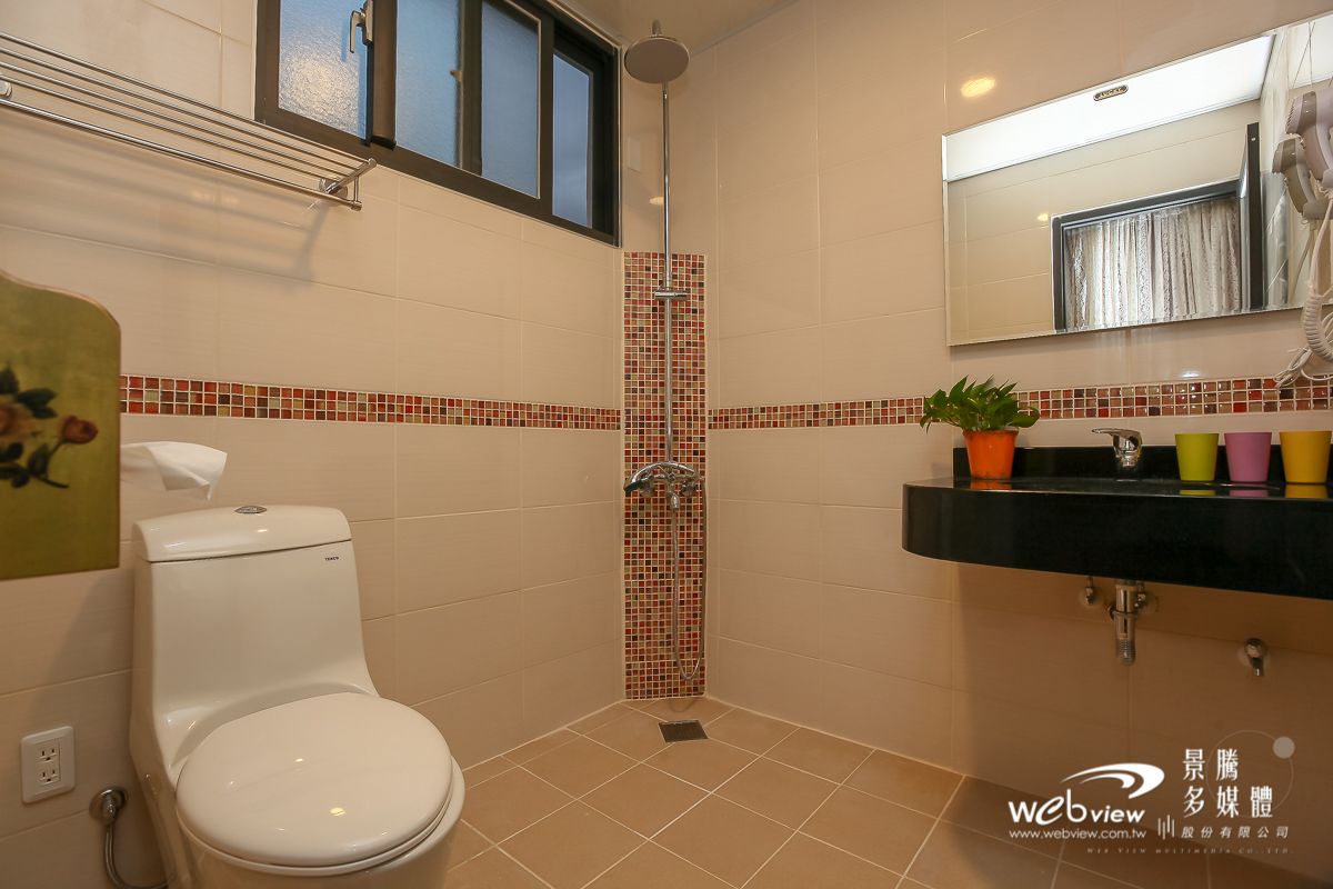 A bathroom with a toilet, a shower with a tiled wall, a sink with a mirror above it, and a potted plant on the sink.