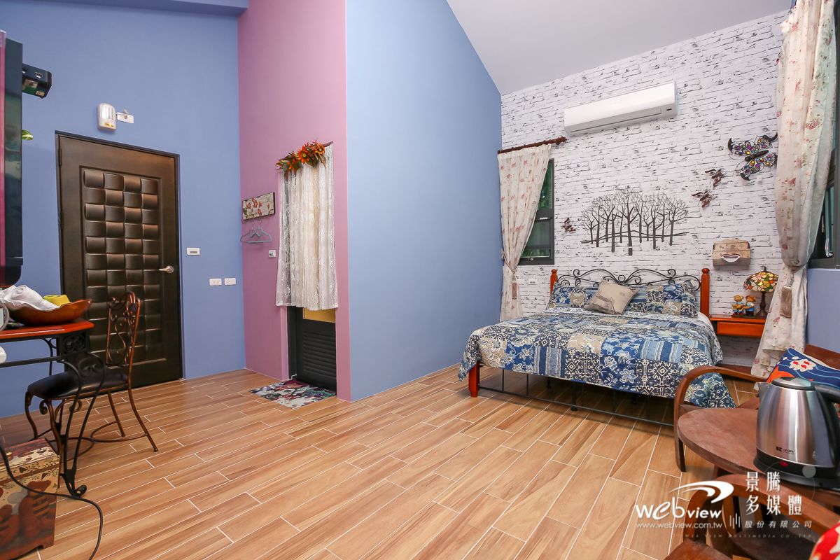 A bedroom with a bed, a desk, and a chair. There is a window with curtains and a wall with a tree mural.