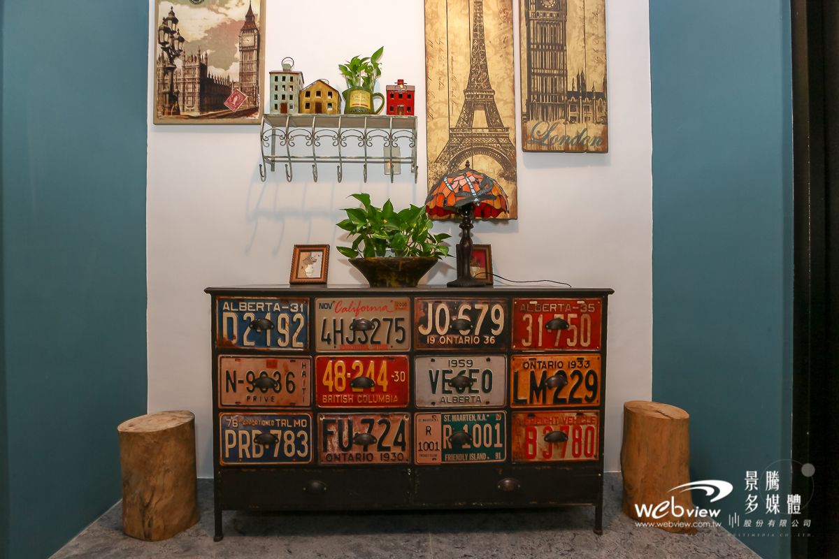 A vintage-style dresser with various license plates, a plant, and a lamp.