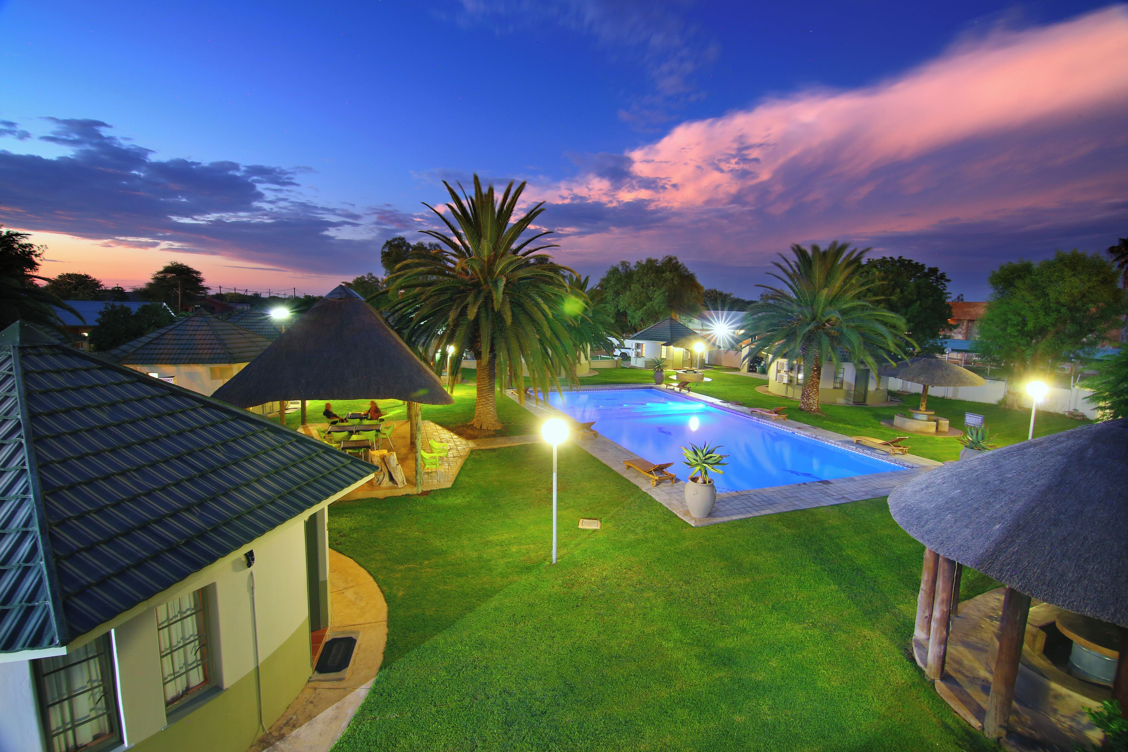 A swimming pool surrounded by well-maintained lawns and palm trees, with houses in the background.