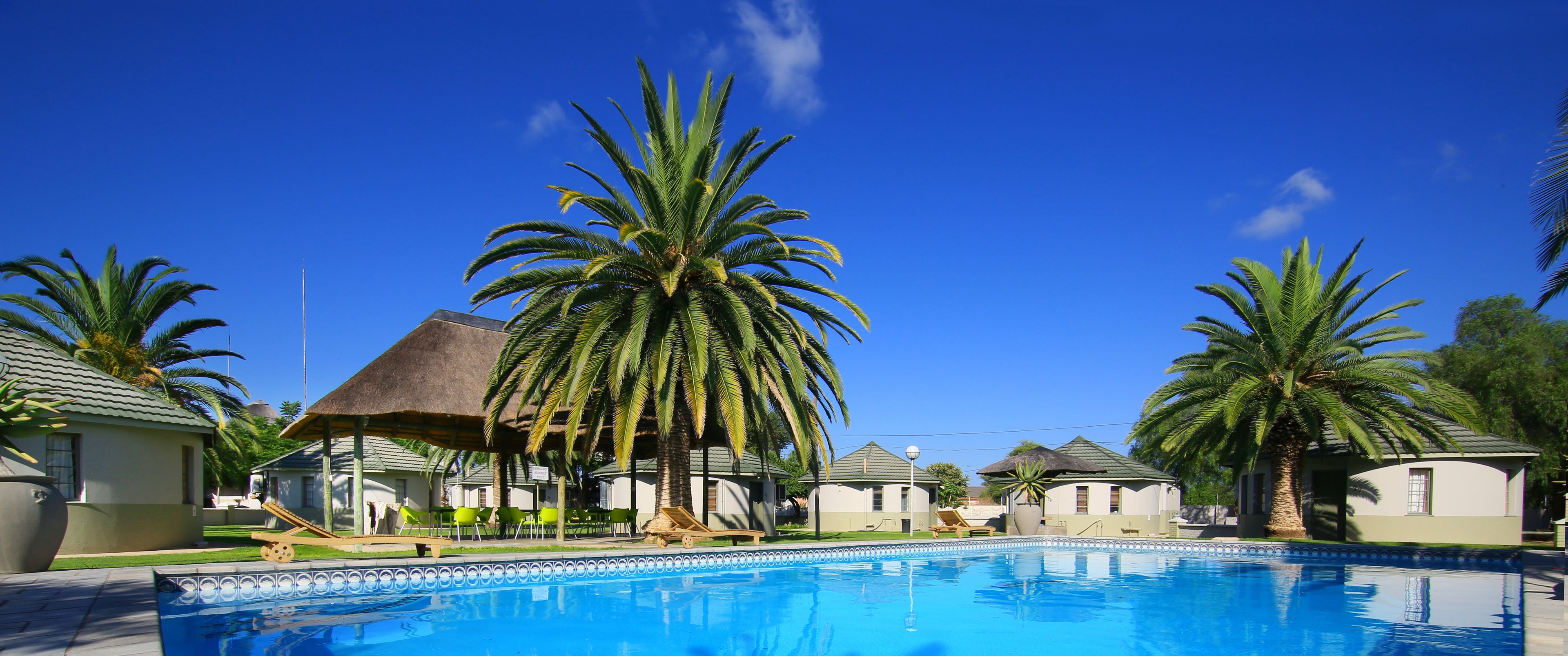 A swimming pool surrounded by palm trees and small buildings with thatched roofs.
