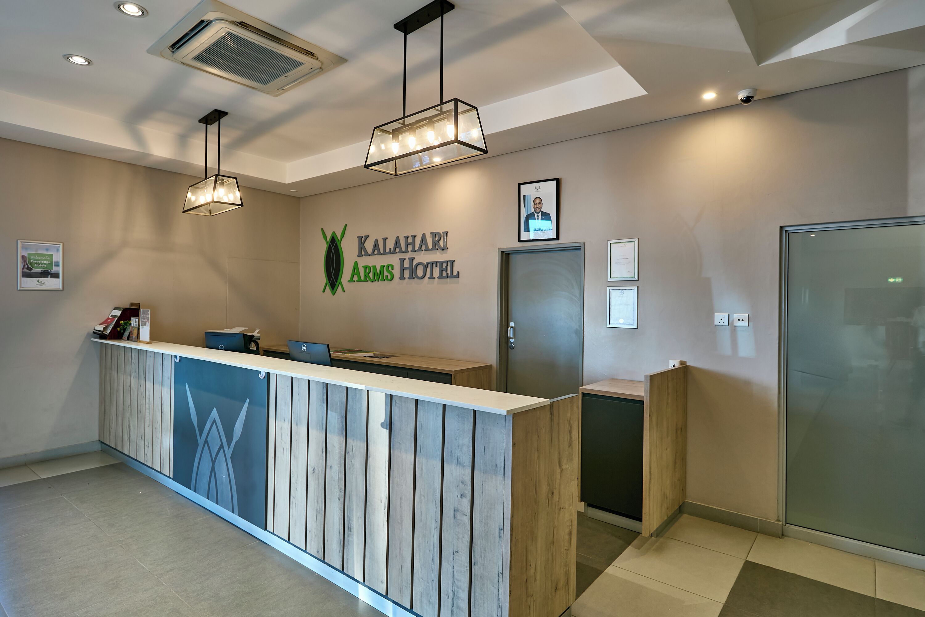 Et receptionområde med en træreception, et indrammet portræt på væggen og et skilt for Kalahari Arms Hotel.