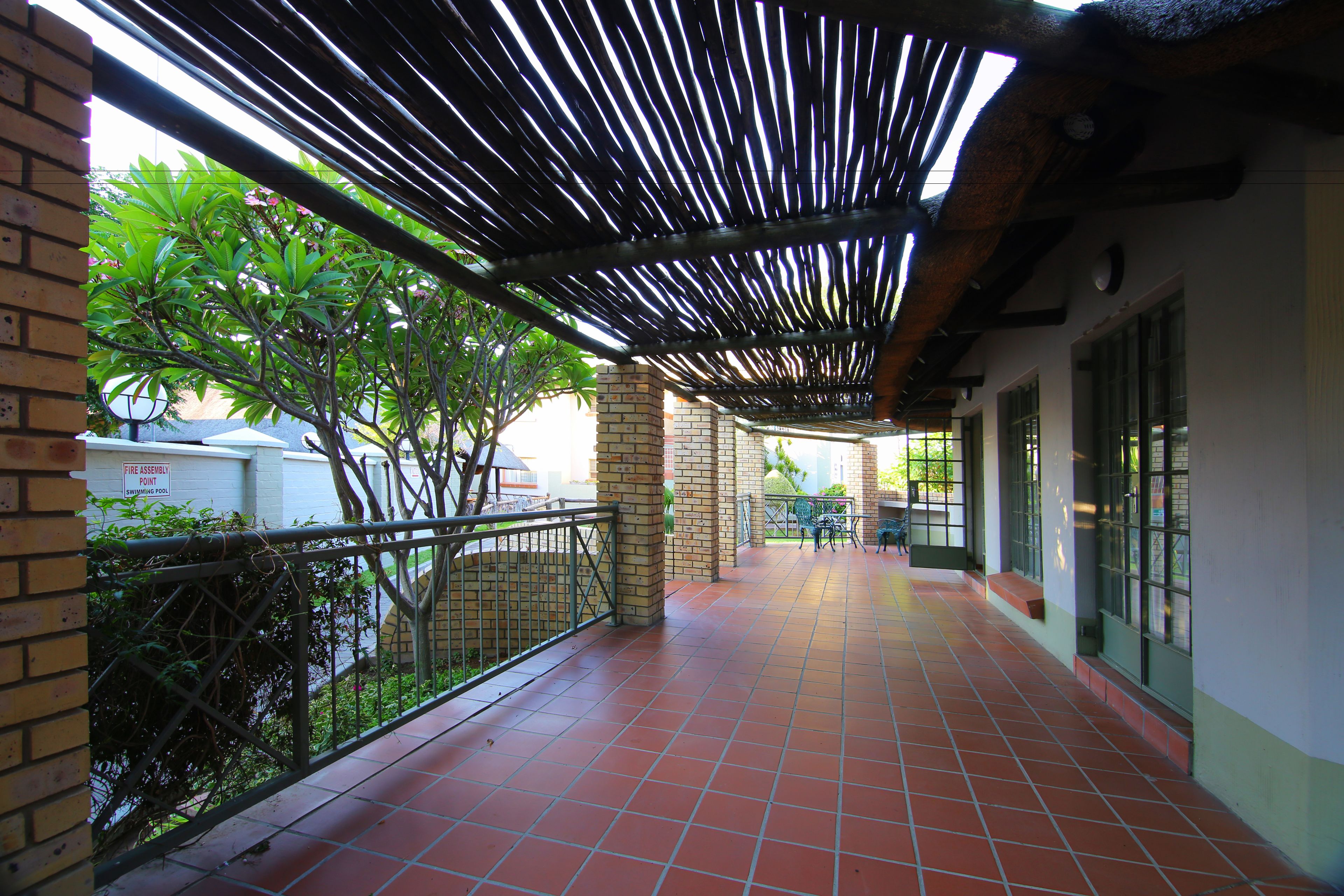 A covered outdoor corridor with tiled flooring, metal railings, and brick pillars.