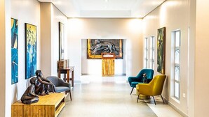A modern lobby with a wooden reception desk, two armchairs, and abstract art on the walls. - Kalahari Arms Hotel (Ghanzi)