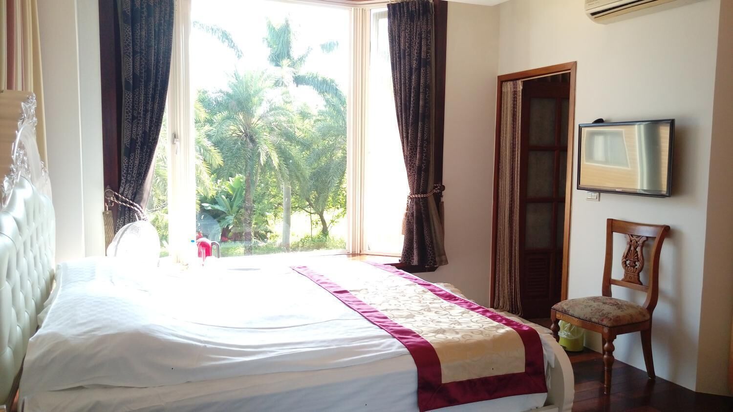 A hotel room with a large bed, a chair, a TV, and a window with curtains.