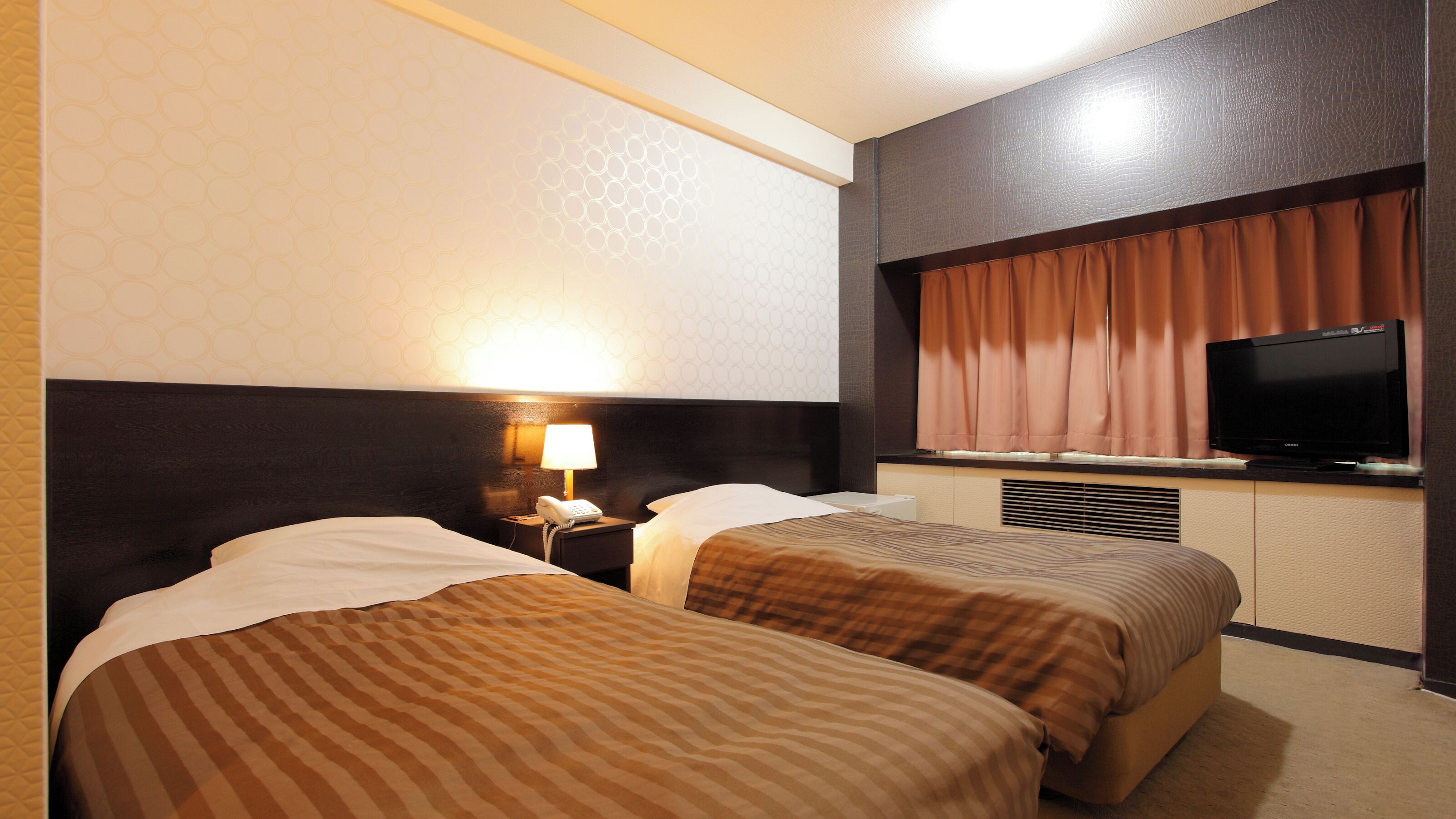 A hotel room with two beds, a TV, a lamp, and a phone on the nightstand.