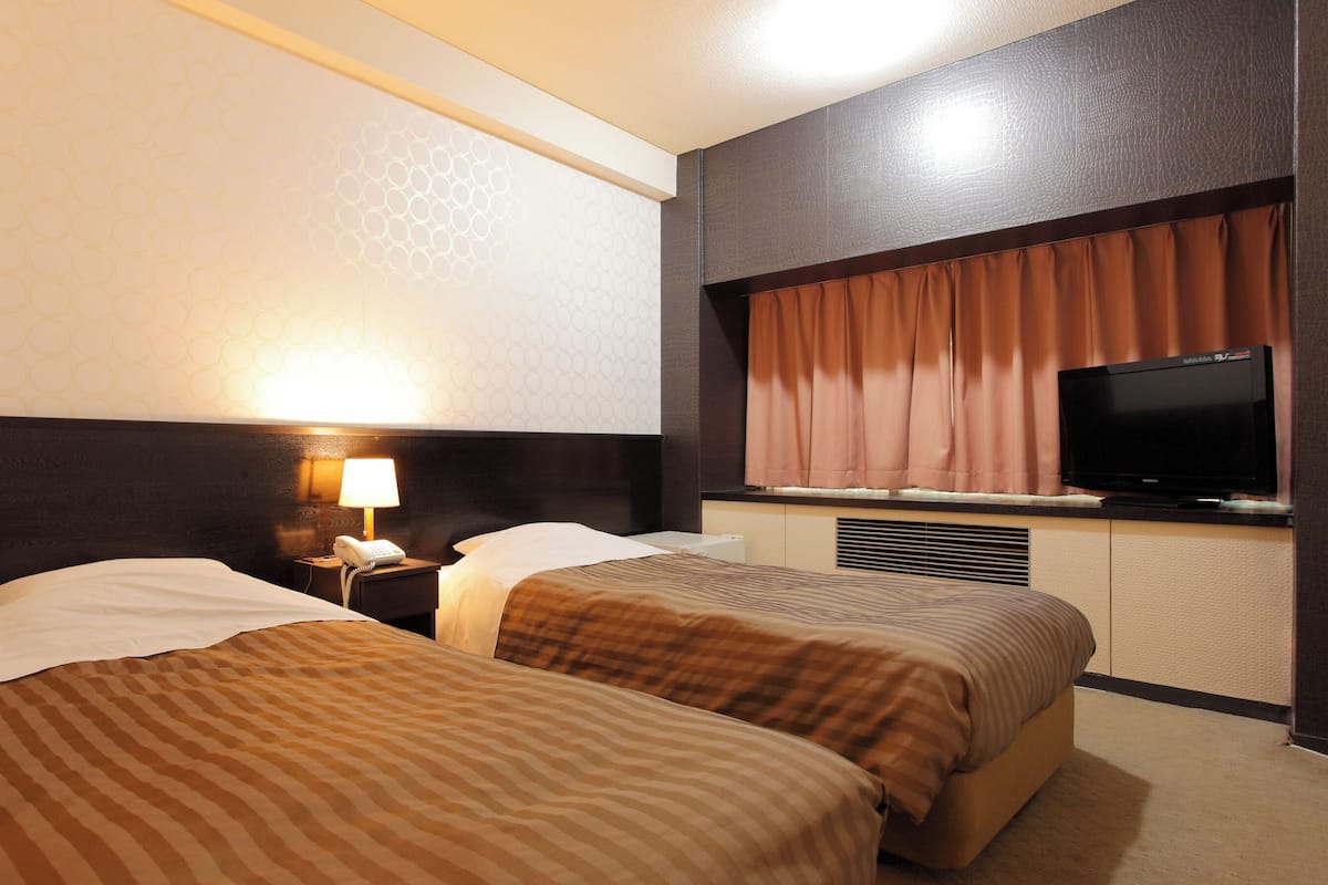 A hotel room with two beds, a TV, a lamp, and a phone on the nightstand.