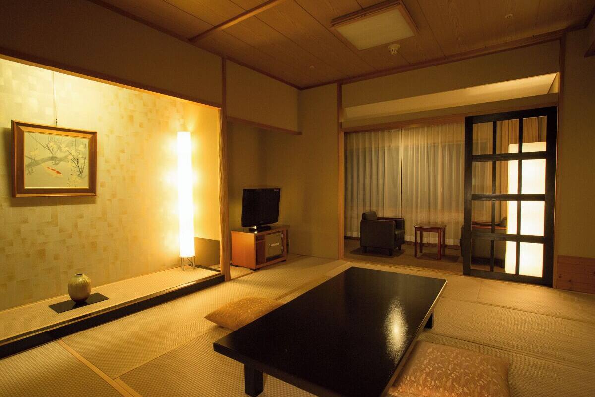 A traditional Japanese room with tatami flooring, a low table, a television, and sliding doors.