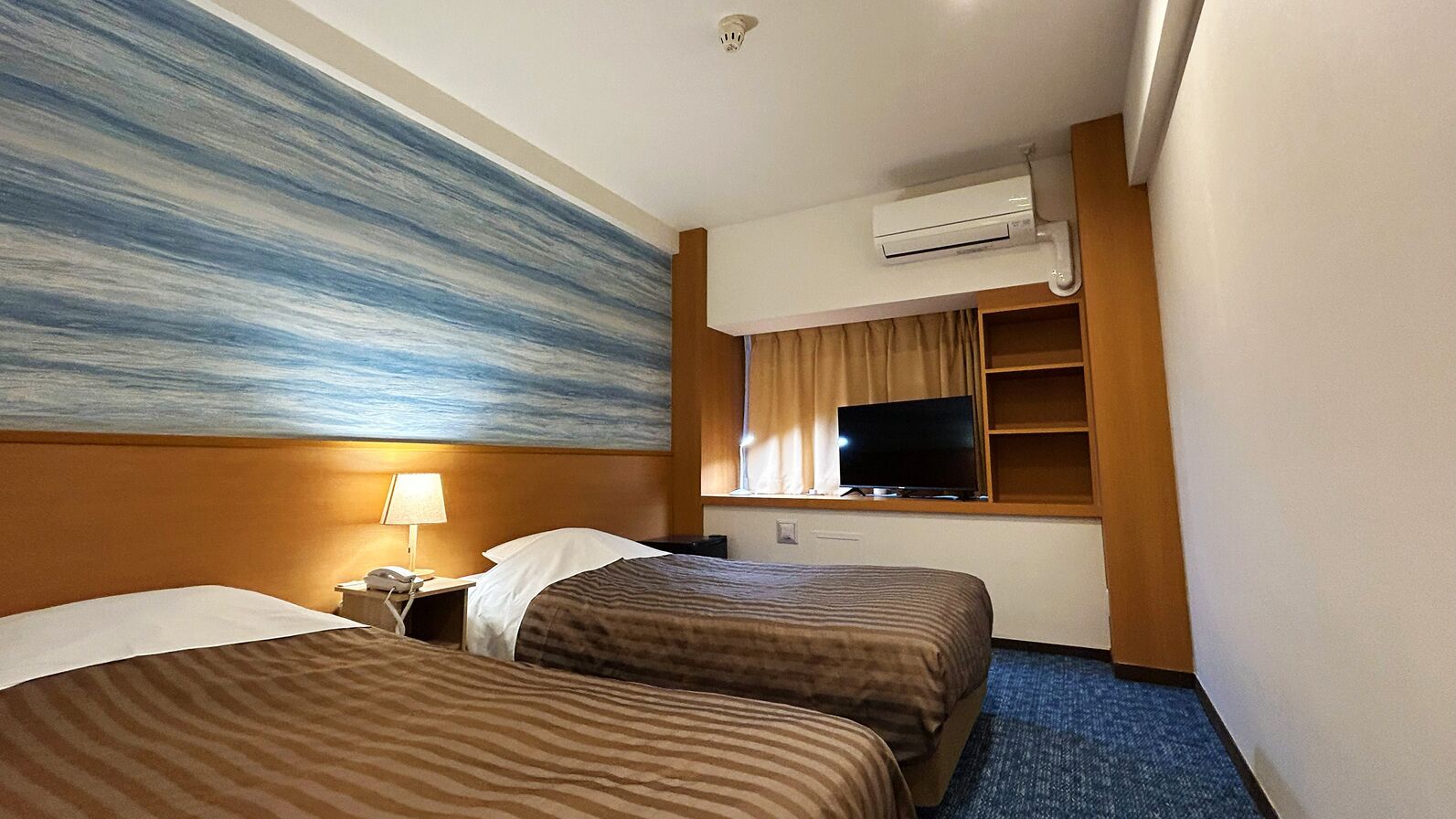 A hotel room with two beds, a television, an air conditioning unit, and a painting on the wall.