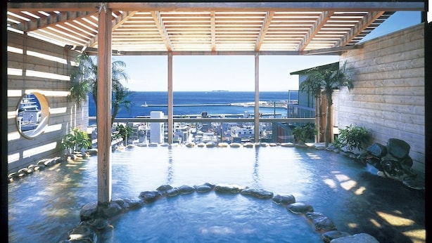 A hot spring area with a wooden pergola, a stone pathway, and a view of the city and ocean. - Atami New Fujiya Hotel (Atami)