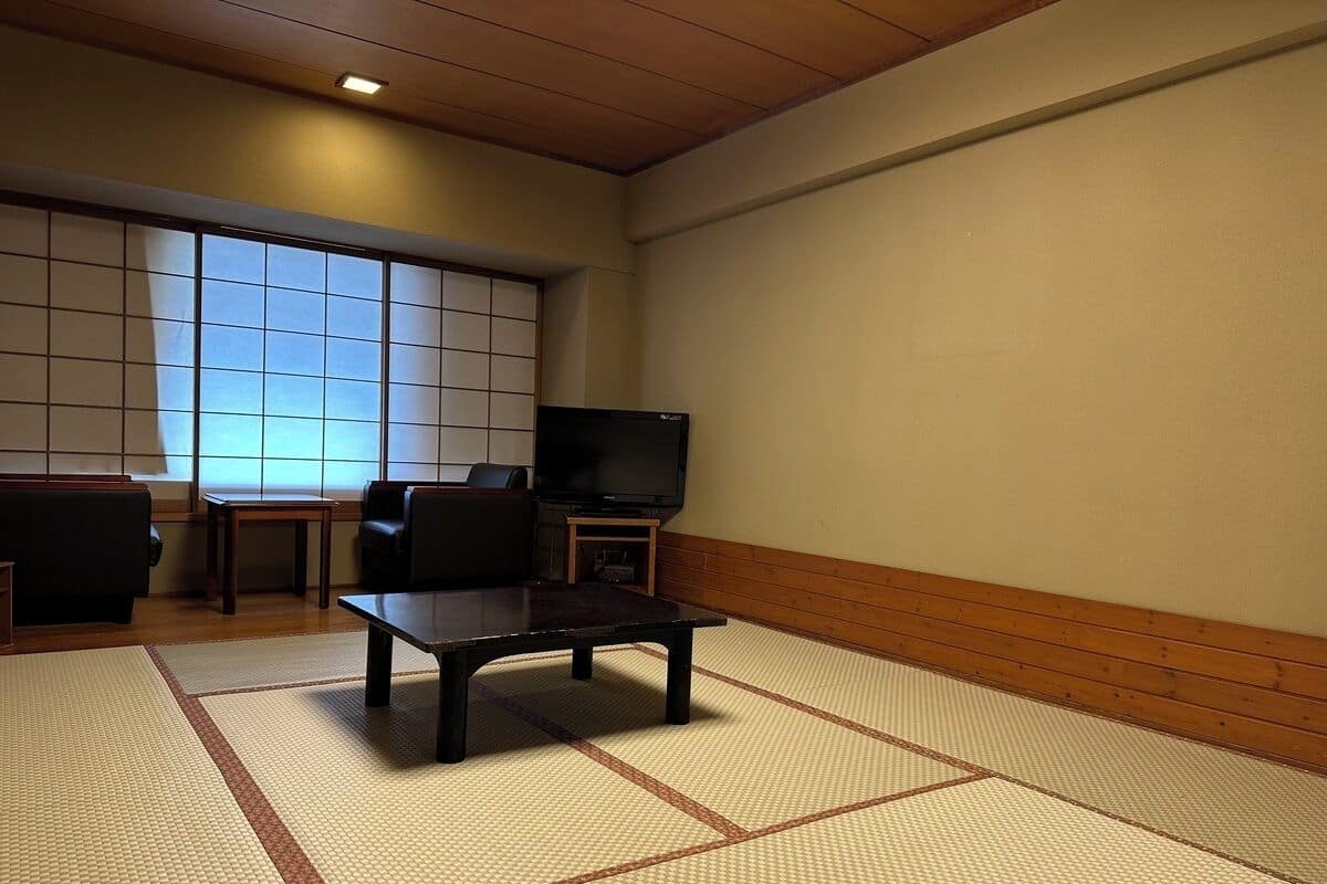 A tatami mat room with a low table, chairs, a television, and a sliding door.
