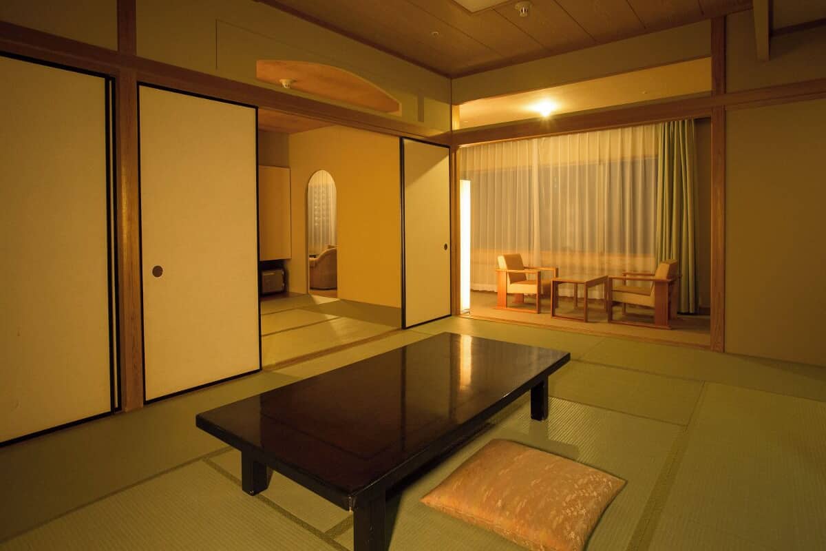 A traditional Japanese room with tatami flooring, a low table, sliding doors, and a seating area with cushions.