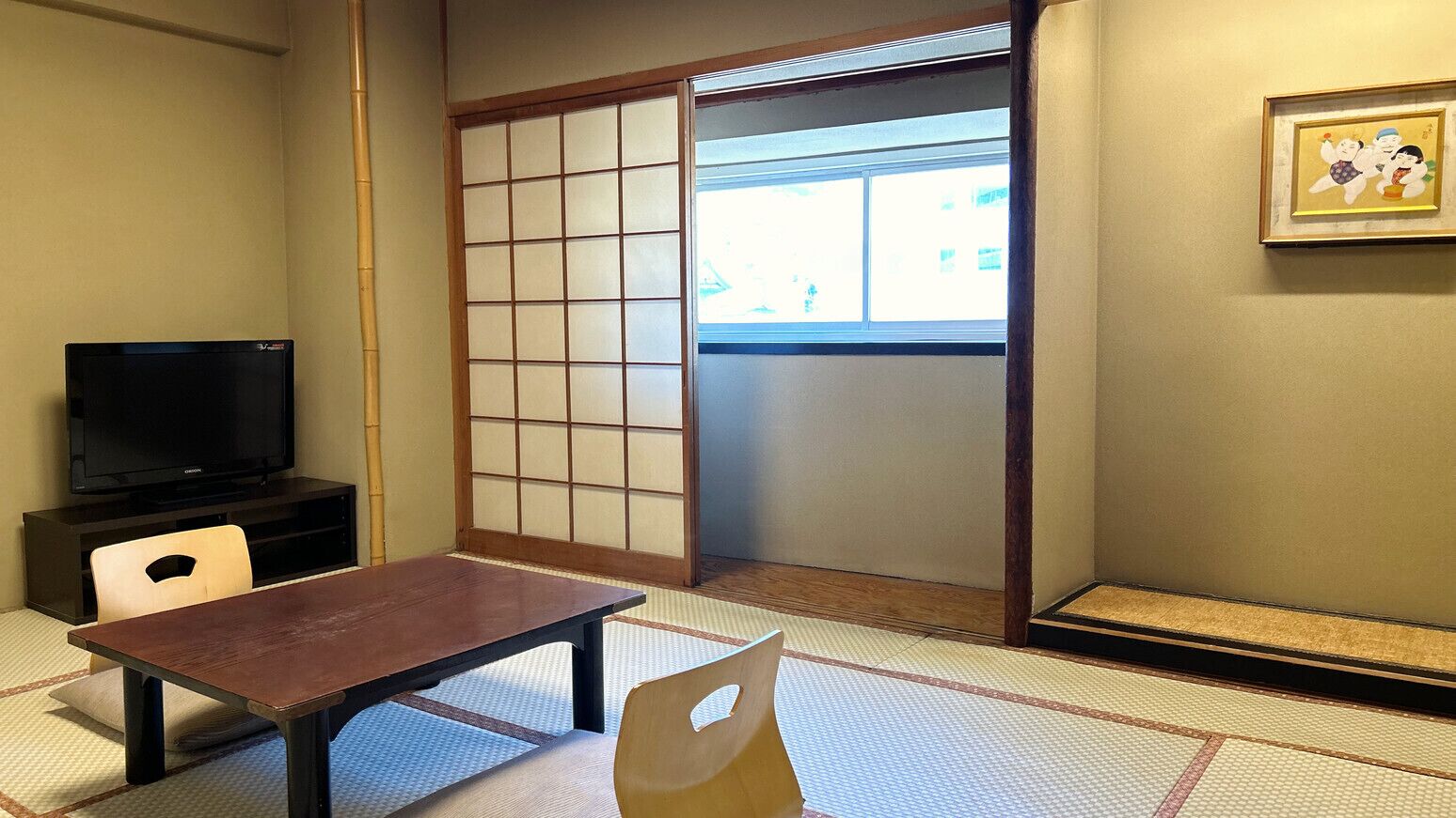 A traditional Japanese room with tatami flooring, a sliding door, a television, and a framed picture on the wall.