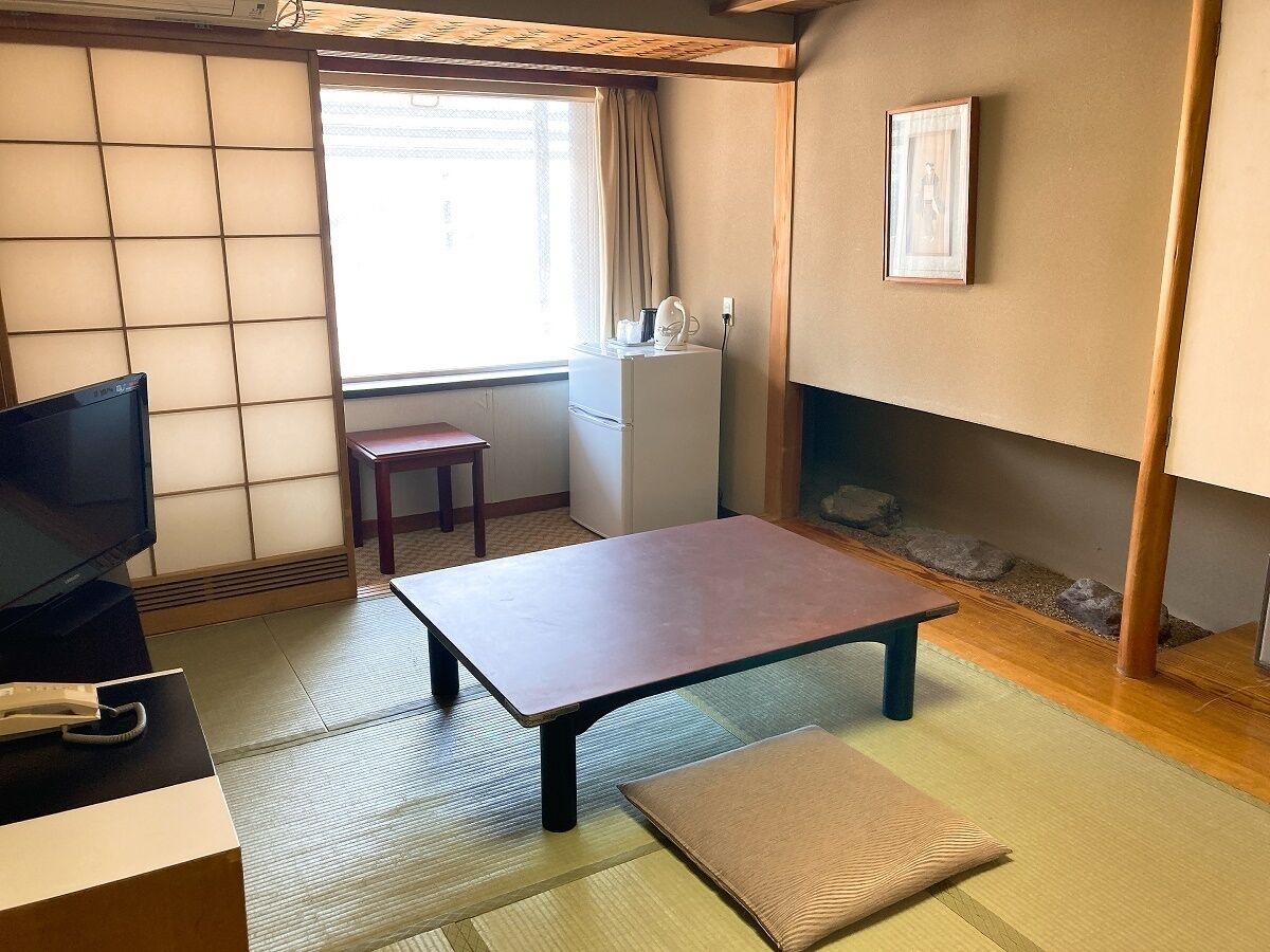 A room with tatami flooring, a low table, a television, a small cabinet, and a framed picture on the wall.