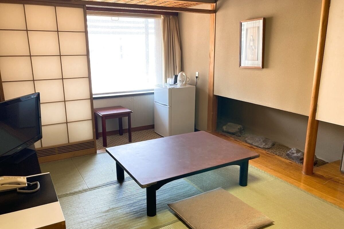 A room with tatami flooring, a low table, a television, a small cabinet, and a framed picture on the wall.