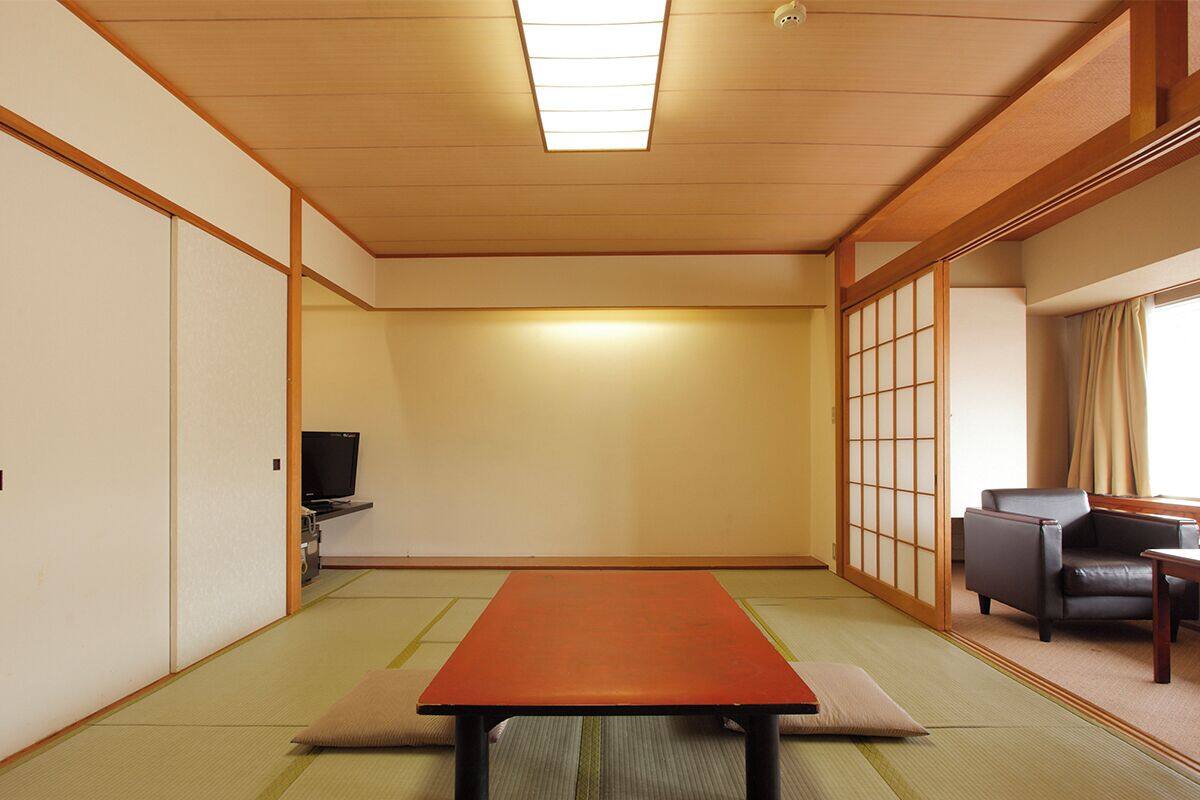 A traditional Japanese room with tatami flooring, a low table, a television, and sliding doors.