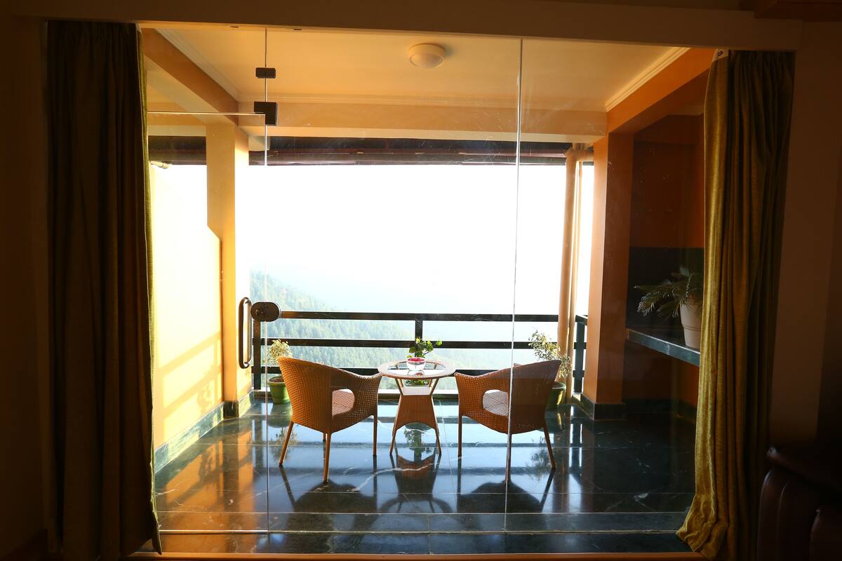 A balcony with two wicker chairs and a small table, overlooking a scenic view.