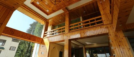 A spacious interior with wooden beams, a balcony, and potted plants.