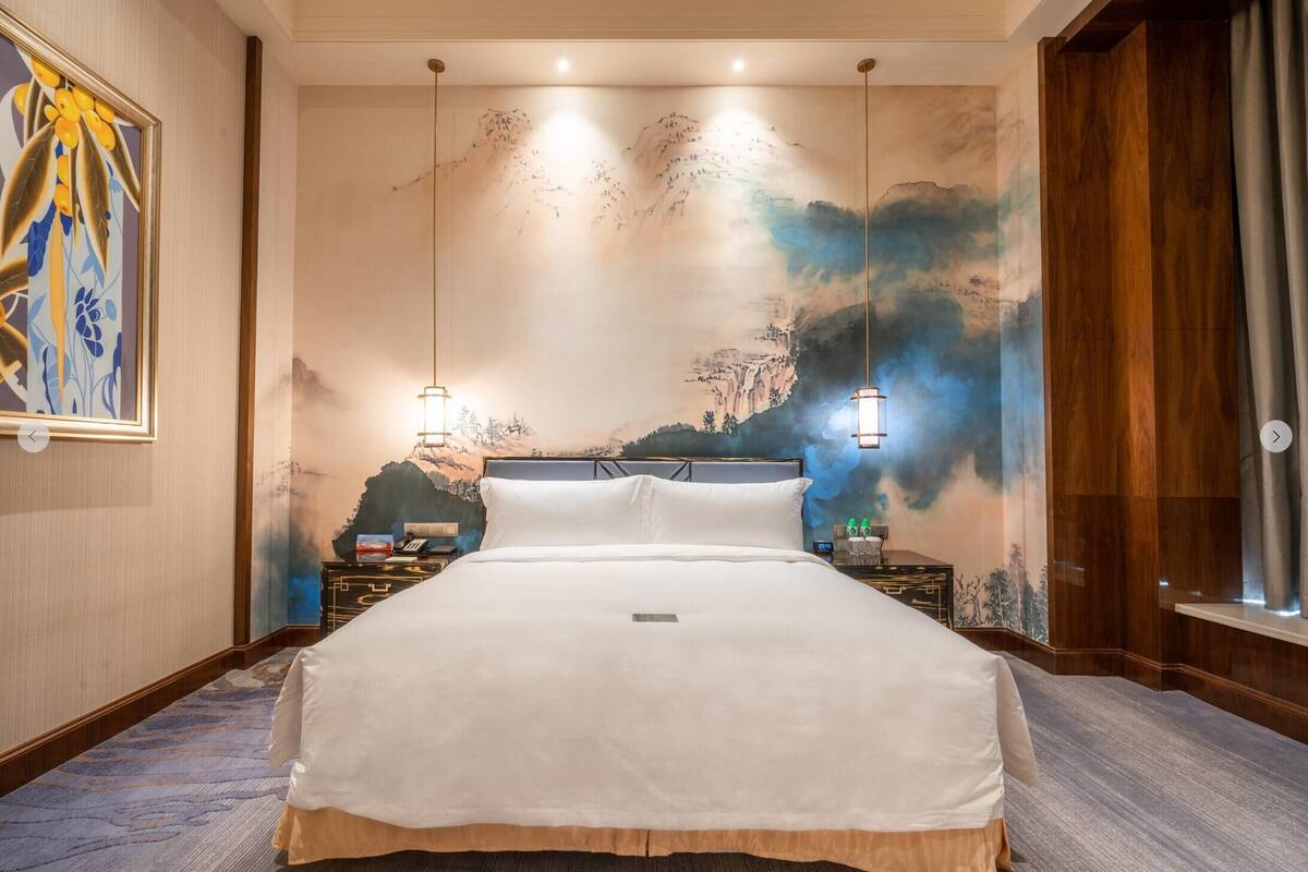 Een hotelkamer met een groot bed, een bergwanddecoratie en twee bedlampjes.
