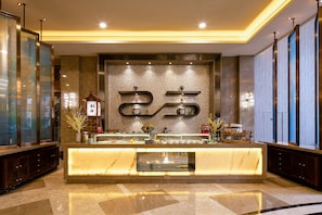A hotel reception area with a marble counter, decorative wall with a large logo, and a traditional Chinese architectural element.