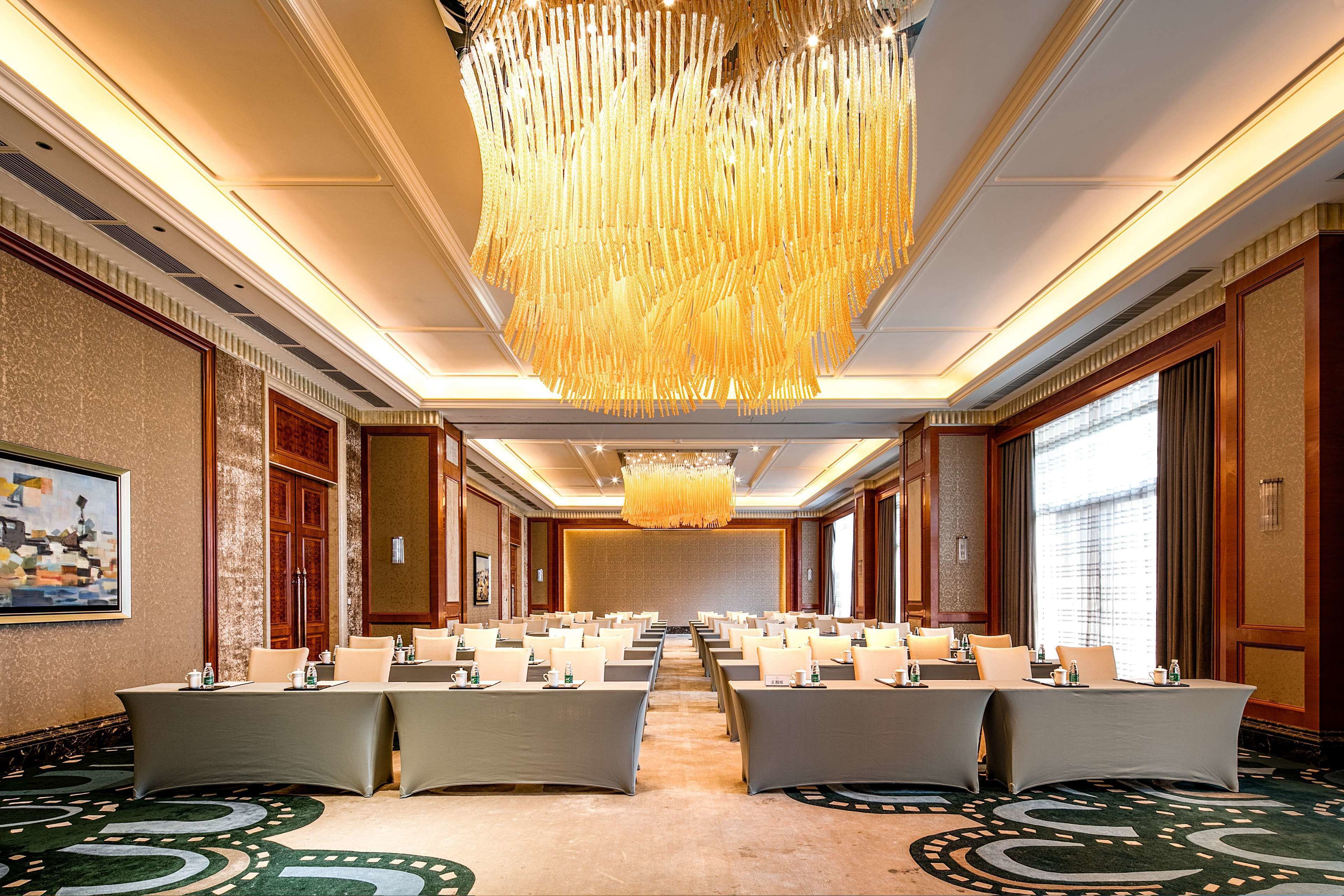 A conference room with long tables, a large chandelier, and a carpeted floor.