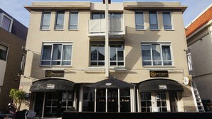 Um edifício com duas placas 'BOUTIQUE SUITES', grandes janelas e toldo preto com a marca 'WARSTEINER'.
