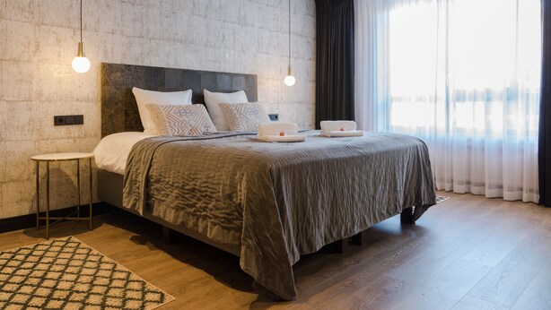 Quarto moderno com uma cama grande, uma mesinha de cabeceira e um lustre suspenso.