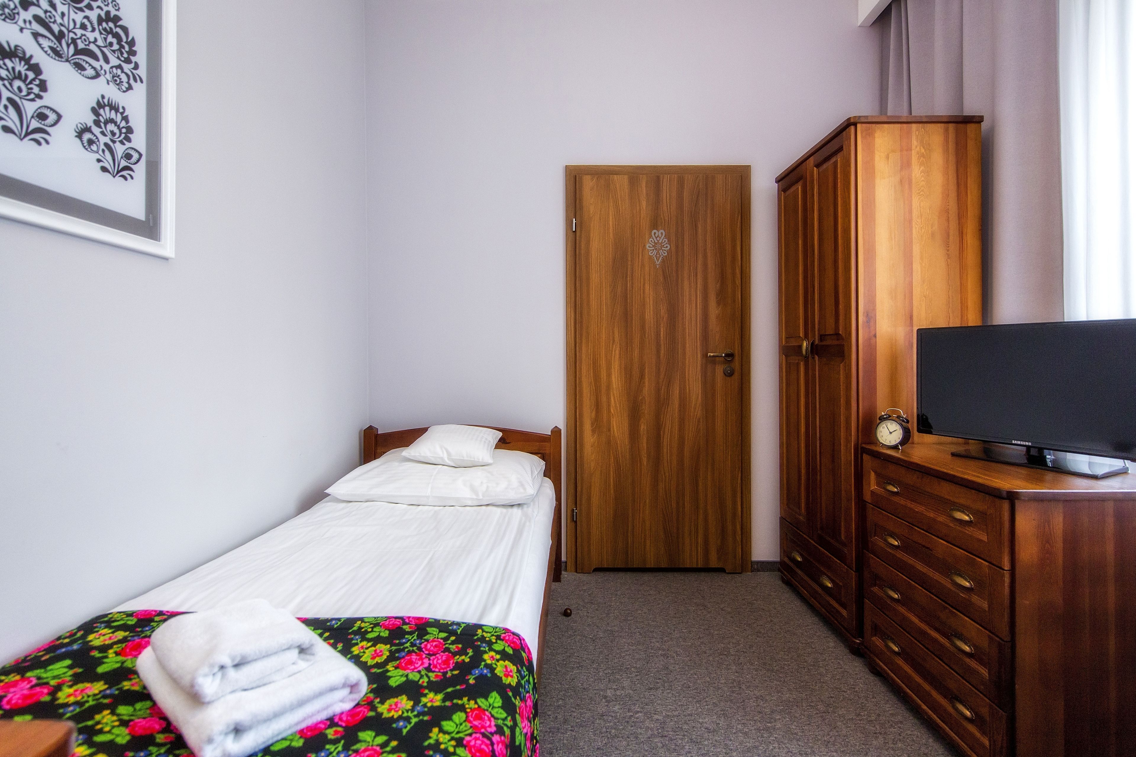 Um quarto com cama, cômoda, televisão e porta.