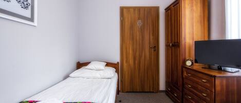 Um quarto com cama, cômoda, televisão e porta.