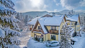 A snow-covered chalet with a balcony, surrounded by snow-laden trees and mountains in the background. - Rezydencja Sienkiewiczówka (Zakopane)