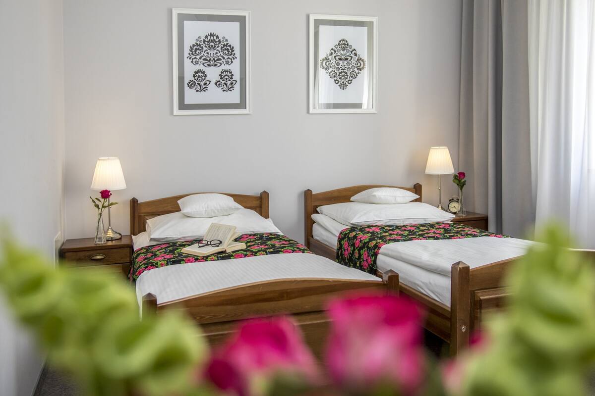 A hotel room with two wooden beds, each with a nightstand, a lamp, and a framed picture on the wall.