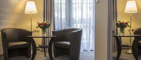 Een moderne hotelkamer met een schuine plafond, twee zwarte lederen fauteuils, een klein rond tafeltje met een bloevas en een lamp.