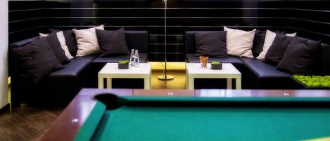 Una mesa de billar en una habitación con un sofá negro y una lámpara.