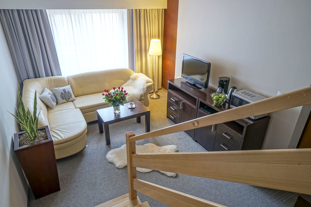 A modern hotel room with a sofa, a coffee table, a TV, and a staircase.