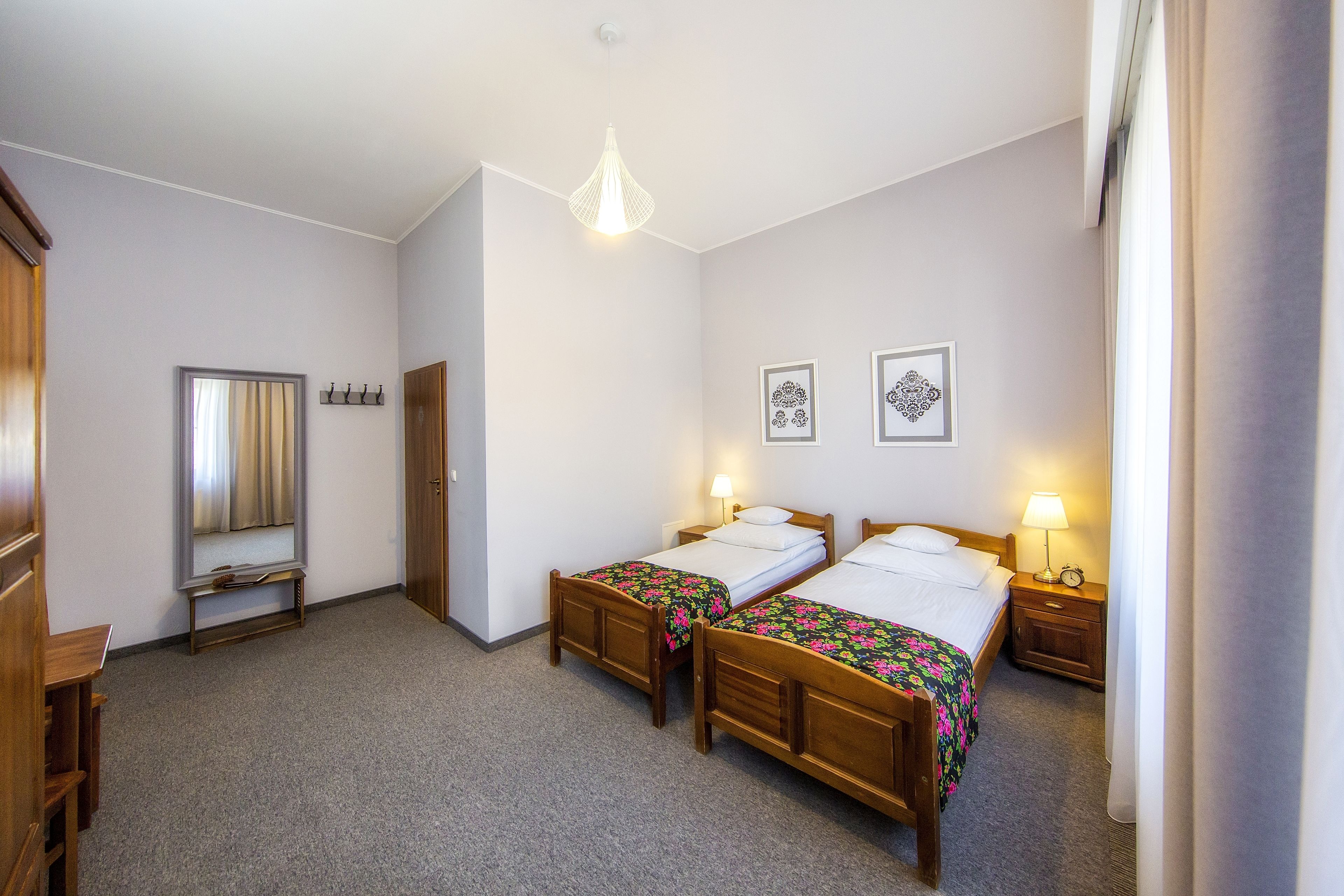 Quarto de hotel com duas camas de madeira, um espelho, um guarda-roupa e uma mesa pequena.