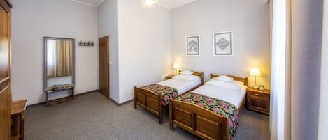 Quarto de hotel com duas camas de madeira, um espelho, um guarda-roupa e uma mesa pequena.