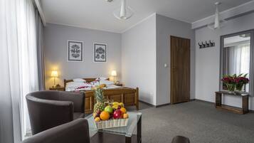 Una habitación de hotel con una cama, una mesa de comedor con fruta, dos sillas, una mesita de noche, una lámpara, un espejo y una puerta.