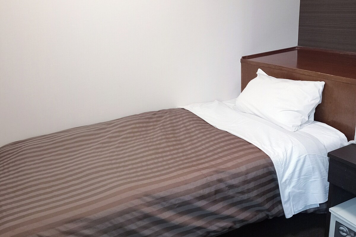 Una cama bien hecha con una colcha a rayas y almohadas blancas, un cabecero de madera y una mesita de noche con una lámpara.