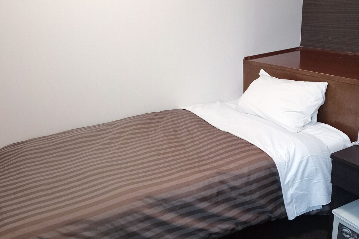 A single bed with a striped bedspread, a white pillow, and a wooden headboard.