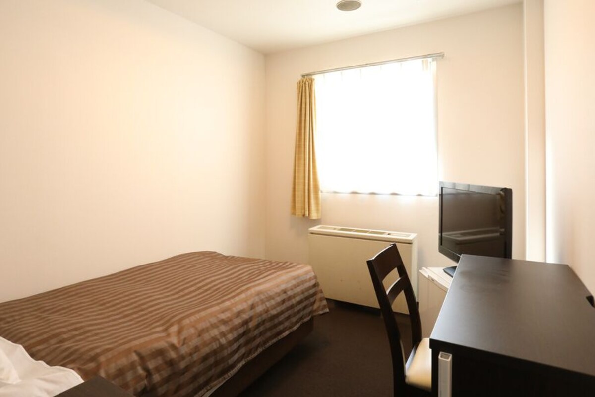 A small, single-bed room with a desk, chair, and a TV.