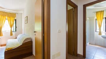 Quarto com cama de madeira, janela com cortinas amarelas e banheiro visível por uma porta aberta.