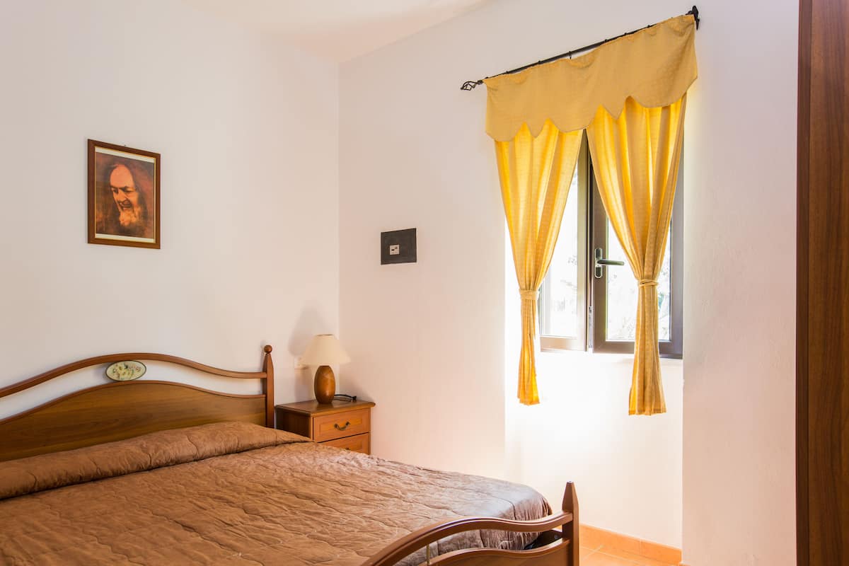 Un dormitorio con una cama de madera, una mesita de noche con lámpara y una ventana con cortinas amarillas.