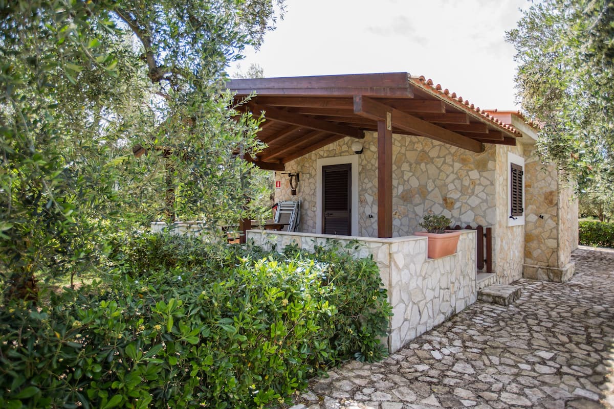 Un edificio de piedra con una pérgola de madera, rodeado de vegetación.